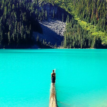 A woman standing on a log partly submerged in a mountain lake.